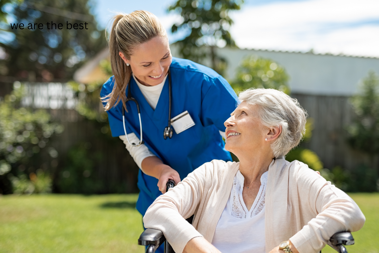 A smiling nurse in blue scrubs and a stethoscope, representing Vital Care Recruiters, assists an elderly woman in a wheelchair outdoors. They are in a garden setting with trees and a fence, while the text “we are the best” graces the top left corner.