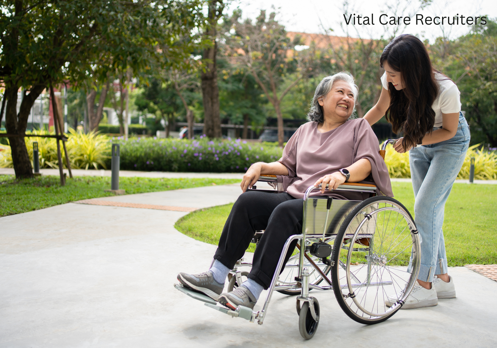 A smiling nurse in white scrubs and a stethoscope, representing Vital Care Recruiters, assists an elderly woman in a wheelchair outdoors. They are in a garden setting with trees and a fence, while the text “we are the best” graces the top left corner.